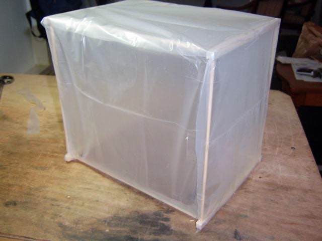 A cube made with bamboo skewers is covered with a transparent drop cloth.