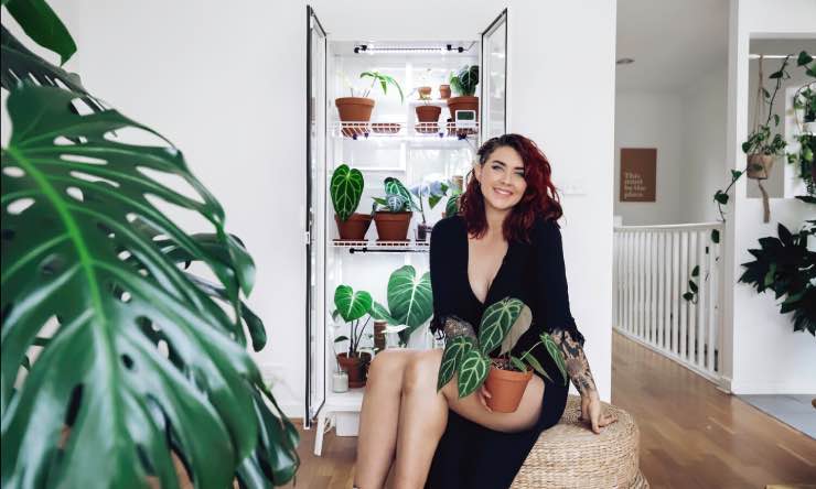 A glass IKEA Milsbo cabinet holds various potted plants. Rachel Aust sits in front of the cabinet.